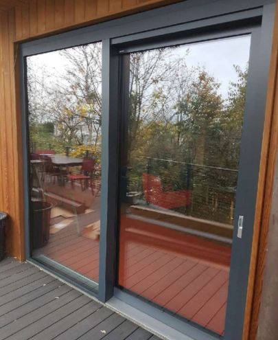 Pose de baie vitrée coulissante gris anthracite sur terrasse en bois à Lyon